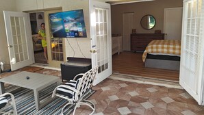 Una habitación con cama, televisor montado en la pared, ventilador de techo y puerta que da a otra estancia.