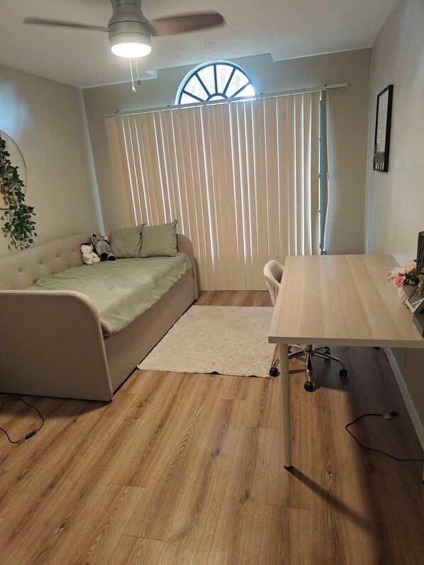 Un dormitorio con cama, escritorio, silla, ventilador de techo y ventana con persianas.