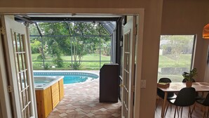 Una puerta abierta que da a un patio con un jacuzzi, una piscina y un comedor con sillas y una mesa.
