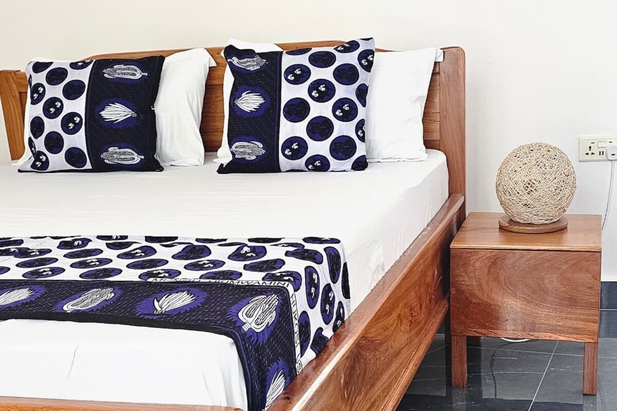 Un lit avec une couvre-lit à motifs, une tête de lit en bois et une table de chevet sur laquelle est posé un objet en fibres tressées.