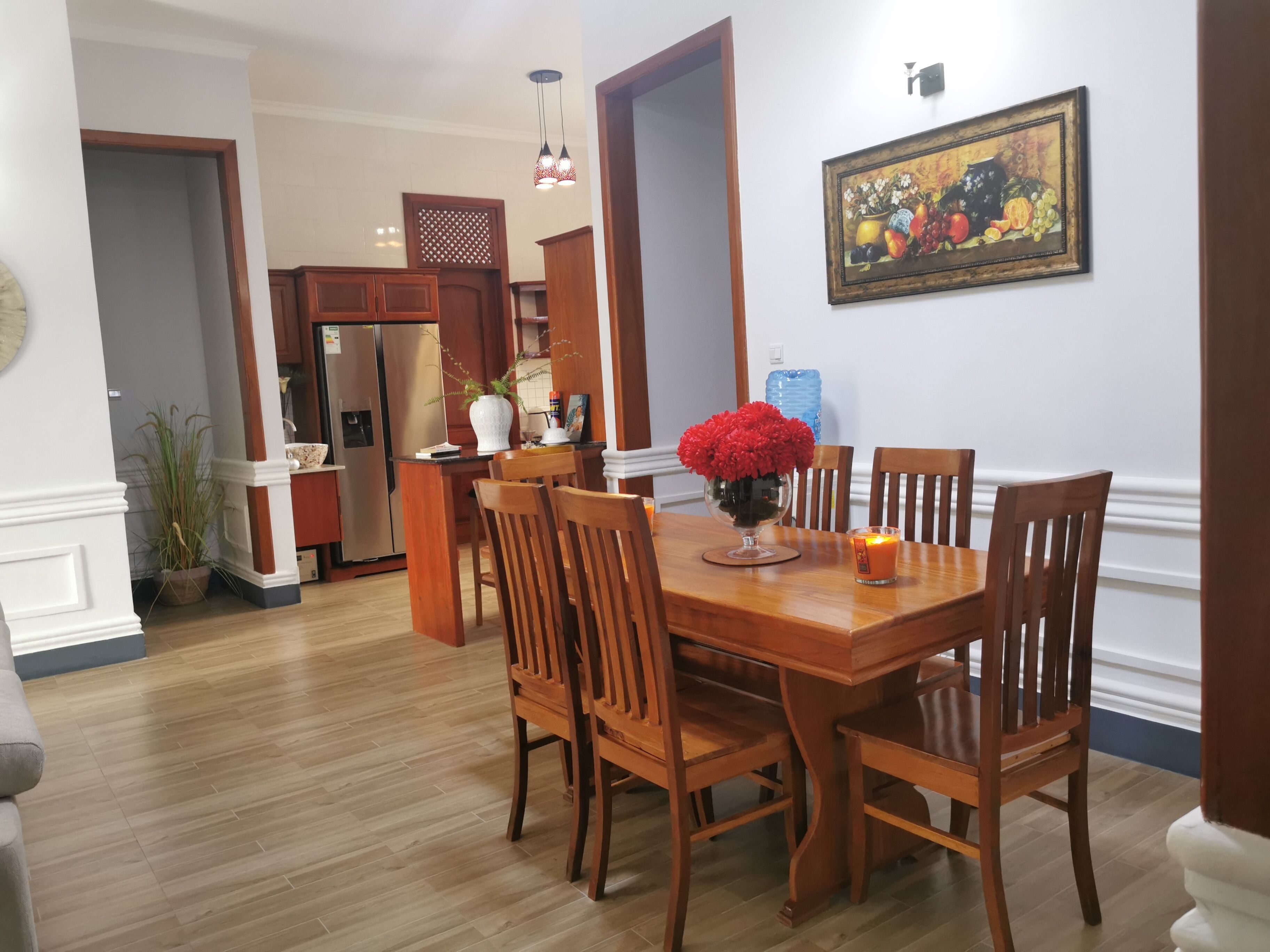 A dining area with a wooden table, chairs, and a vase of red flowers.