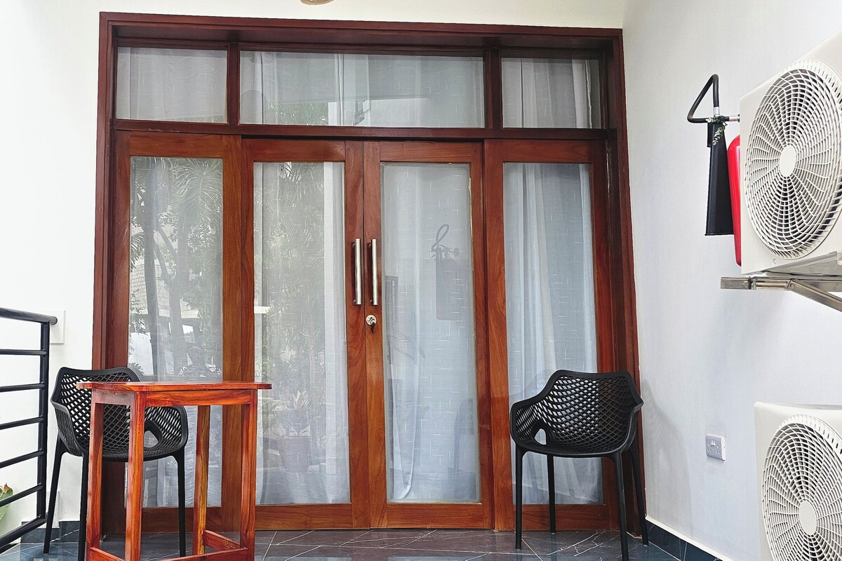 Una habitación con puerta de madera, dos sillas, una mesita y dos ventiladores de pared.