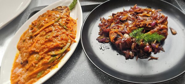 Deux assiettes, chacune contenant un plat différent : l’une avec une sauce et des légumes, l’autre avec des oignons caramélisés et des herbes.