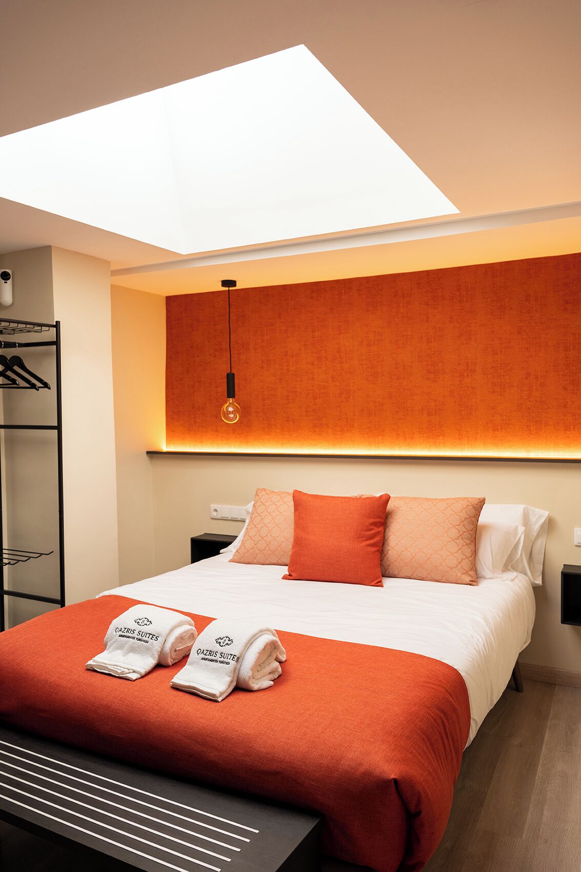 Een hotelkamer met dakraam, een bed met oranje beddengoed, een nachtkastje en een hanglamp.