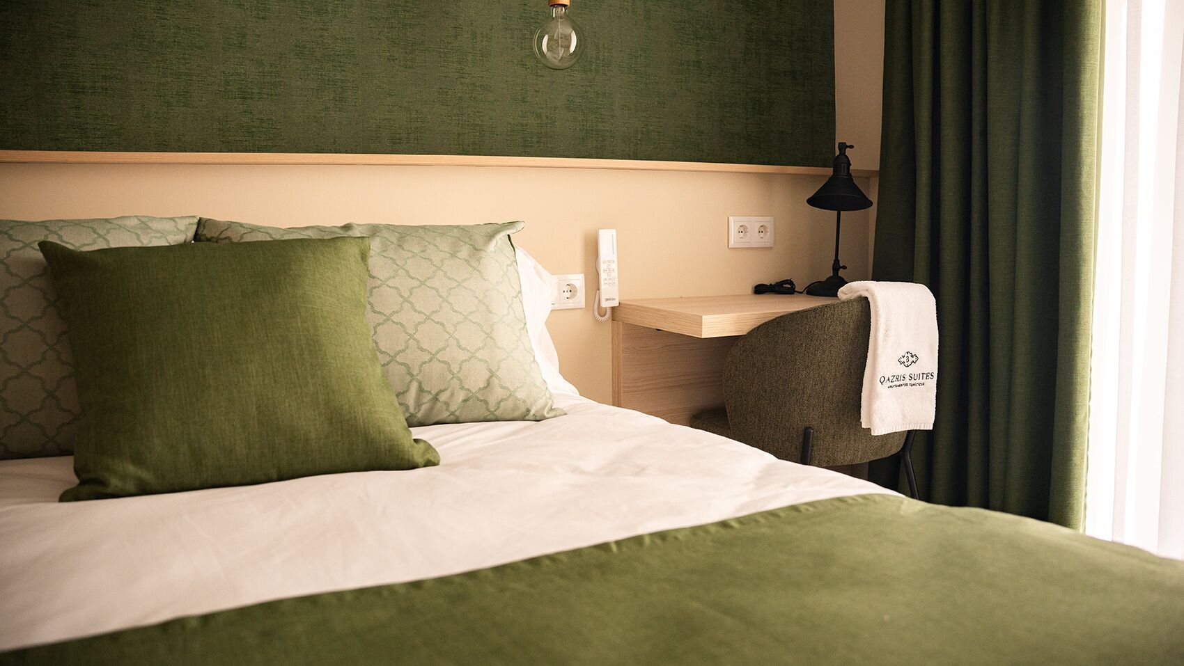 A hotel room with a bed, a nightstand, a lamp, and a window with curtains.