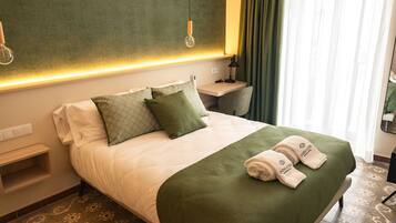 A hotel room with a neatly made bed, a bedside table, a lamp, and a view of the outside through the window.