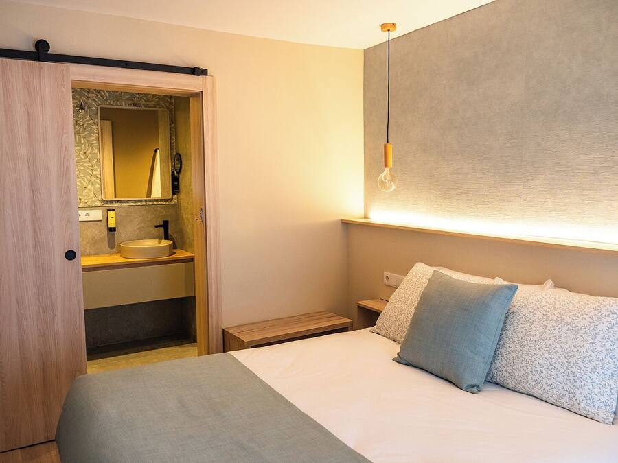 Habitación de hotel con cama, mesita de noche y armario empotrado con espejo y lavamanos.
