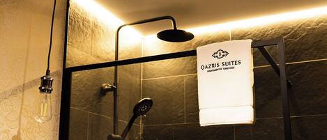 Ein Duschbereich mit Glastür, ein Handtuch, das an der Tür hängt, und ein Schild mit der Aufschrift 'QAZRIS SUITES APARTAMENTOS TURISTICOS'.