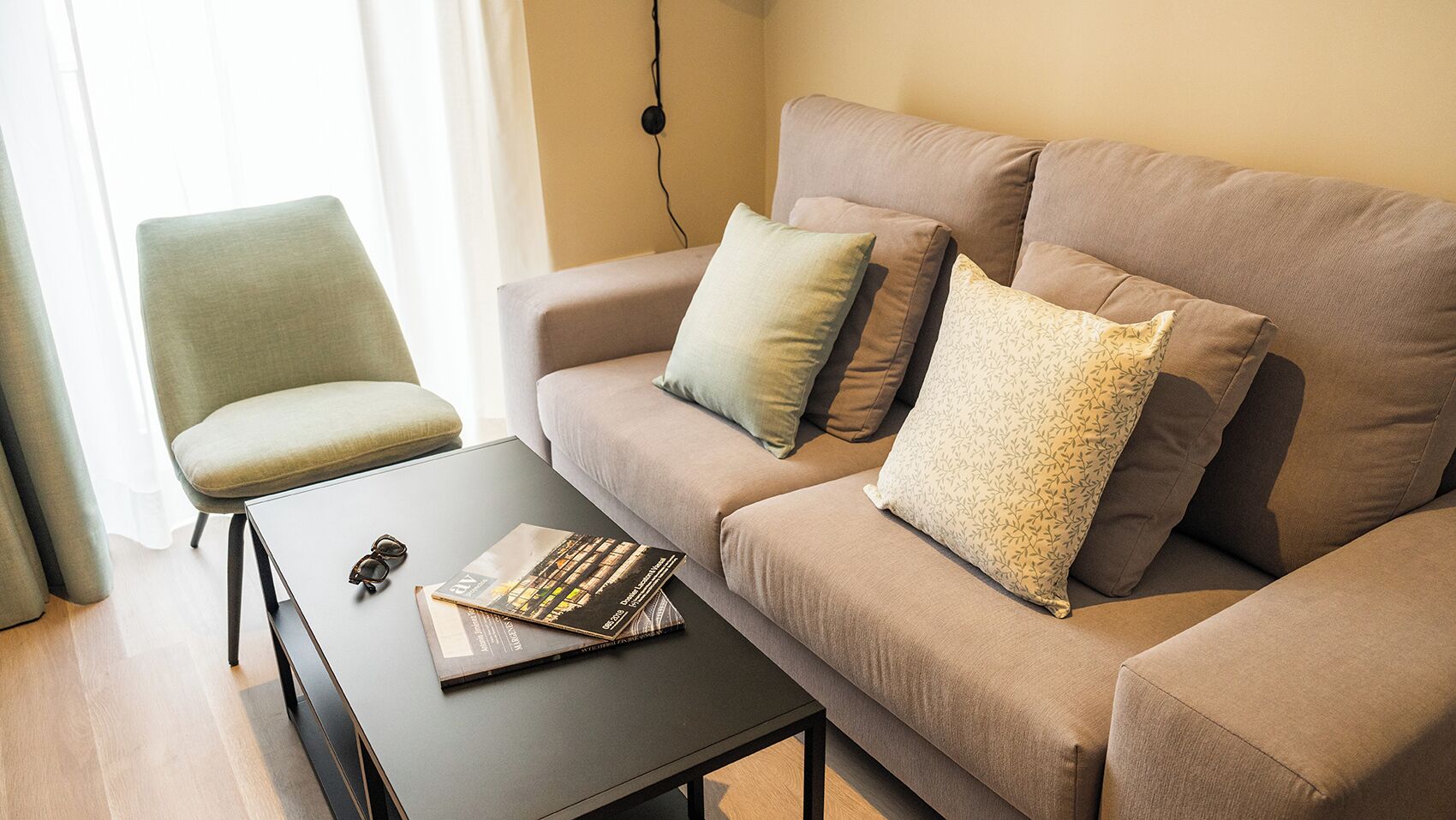 A modern living room with a beige sofa, a green armchair, and a black coffee table.