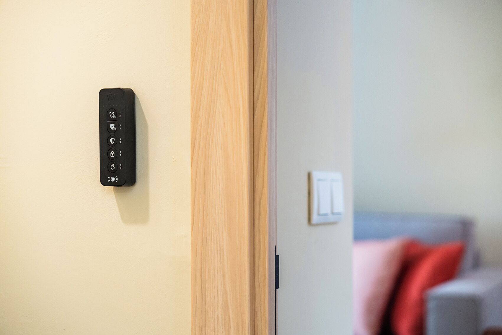 Un panneau de commande fixé au mur, orné de divers pictogrammes, une porte avec un cadre en bois et un interrupteur sur le mur.