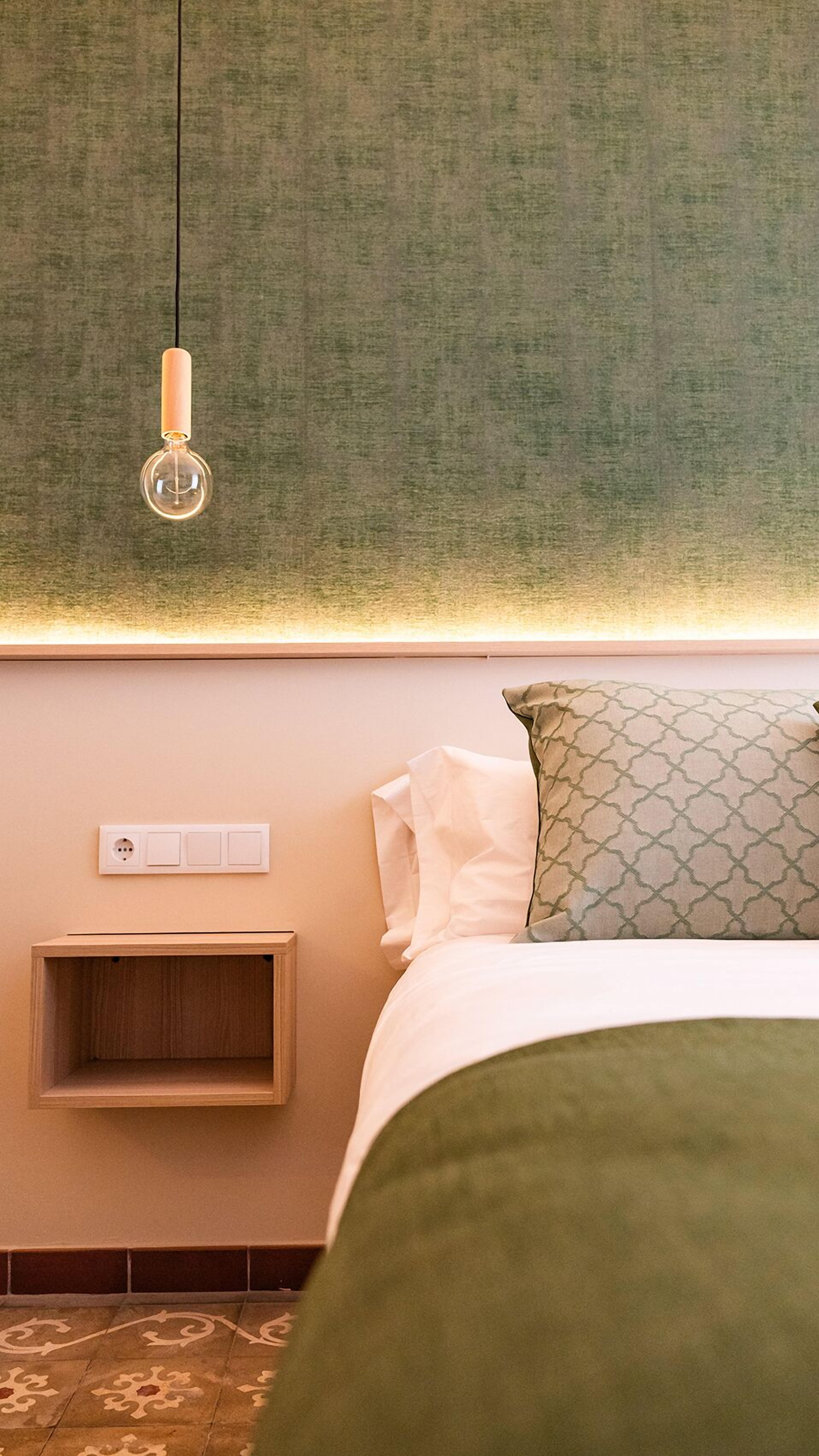 Quarto com cama, mesa de cabeceira, tomada na parede e luminária pendente.