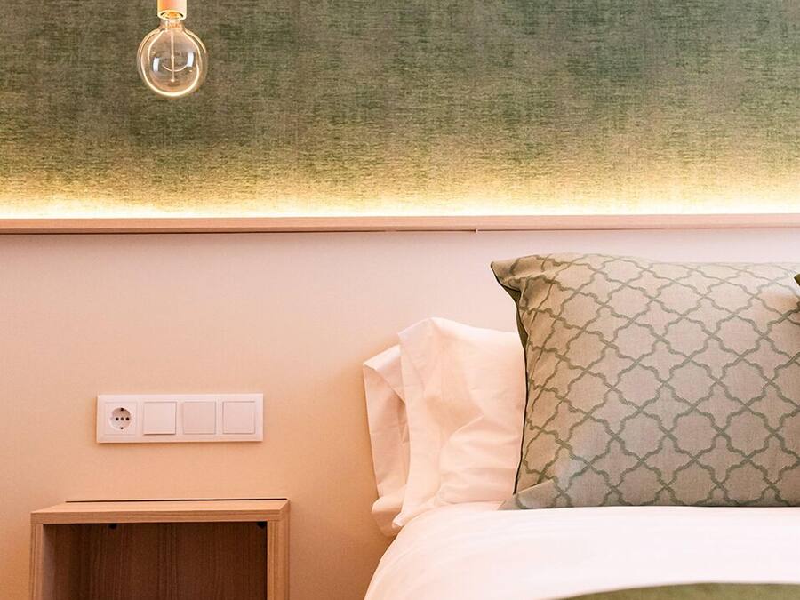 Quarto com cama, mesa de cabeceira, tomada na parede e luminária pendente.