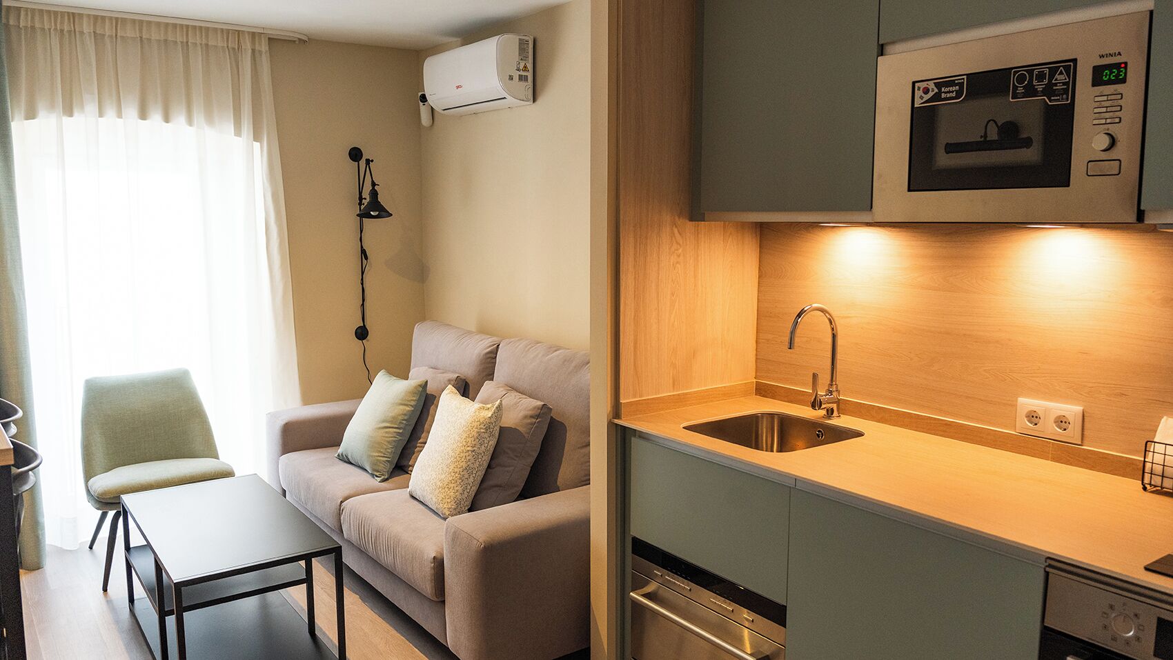 A compact living space with a kitchenette, a sofa with cushions, a small dining table, and a lamp.