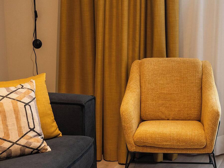 A modern living room with a dark sofa, a mustard-colored armchair, and a black coffee table with a wireframe base.