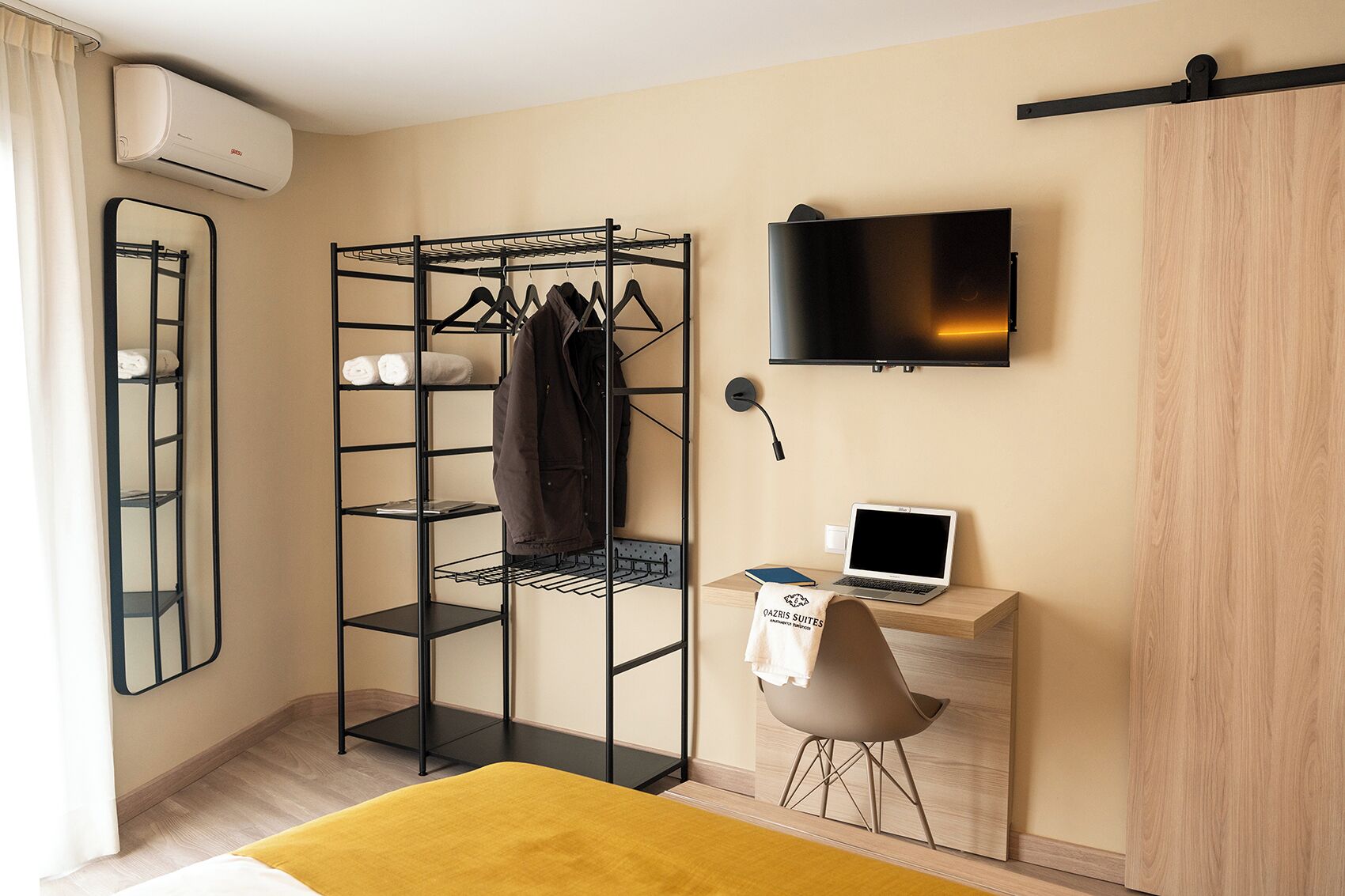 Une chambre d’hôtel avec un placard, un bureau avec un ordinateur portable, une télévision et un lit recouvert d’une couverture jaune.