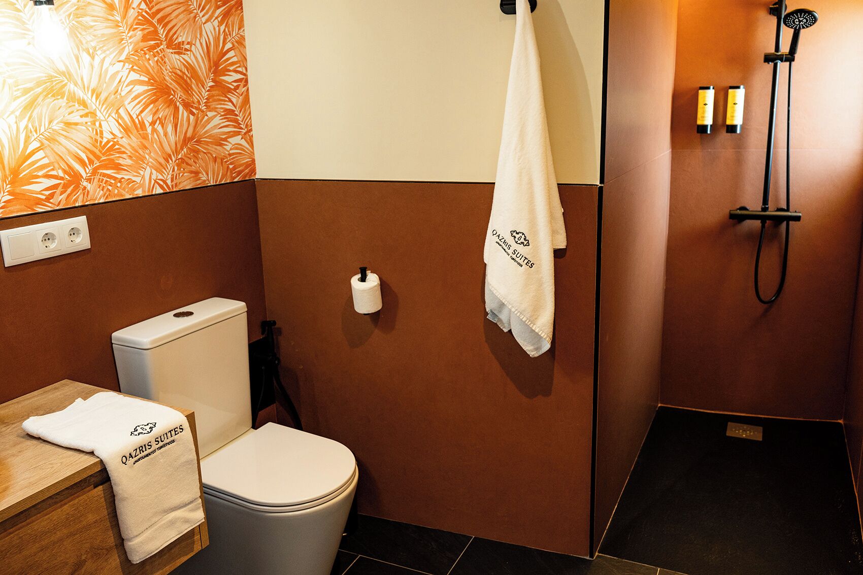 Un baño con inodoro, toallero con toalla, ducha y dispensador de papel higiénico.