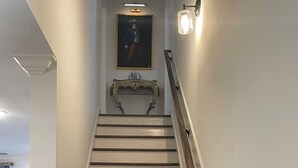A staircase with wooden steps and a handrail, leading to a landing with a framed artwork and a wall-mounted light fixture.