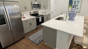 A modern kitchen with stainless steel appliances, a white countertop, and a patterned rug.