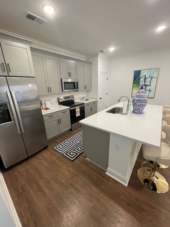 A modern kitchen with stainless steel appliances, a white countertop, and a patterned rug.