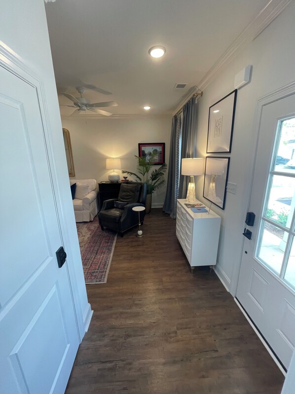 A hallway with a ceiling fan, a seating area with a couch and chairs, a small table with a lamp, and a window with curtains.