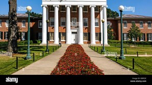 A building with a central entrance flanked by columns, surrounded by a well-maintained lawn and a pathway leading to it.