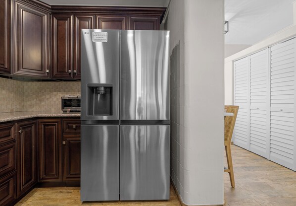 Un refrigerador de acero inoxidable en una cocina con armarios de madera oscura y una puerta blanca.