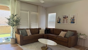 A modern living room with a brown sectional sofa, a round coffee table, and a potted plant. - Desert Getaway Home 4 bed and 2 bath with luxurious upgrades (Palm Desert)