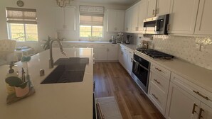A modern kitchen with white cabinetry, a stainless steel range hood, and a large island with a sink. - Desert Getaway Home 4 bed and 2 bath with luxurious upgrades (Palm Desert)