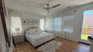 A bedroom with a bed, a ceiling fan, a nightstand with a lamp, and a view of the outside through a door. - Desert Getaway Home 4 bed and 2 bath with luxurious upgrades (Palm Desert)