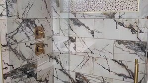 Ducha con cerramiento de vidrio, azulejos de mármol y piso con diseño de guijarros.