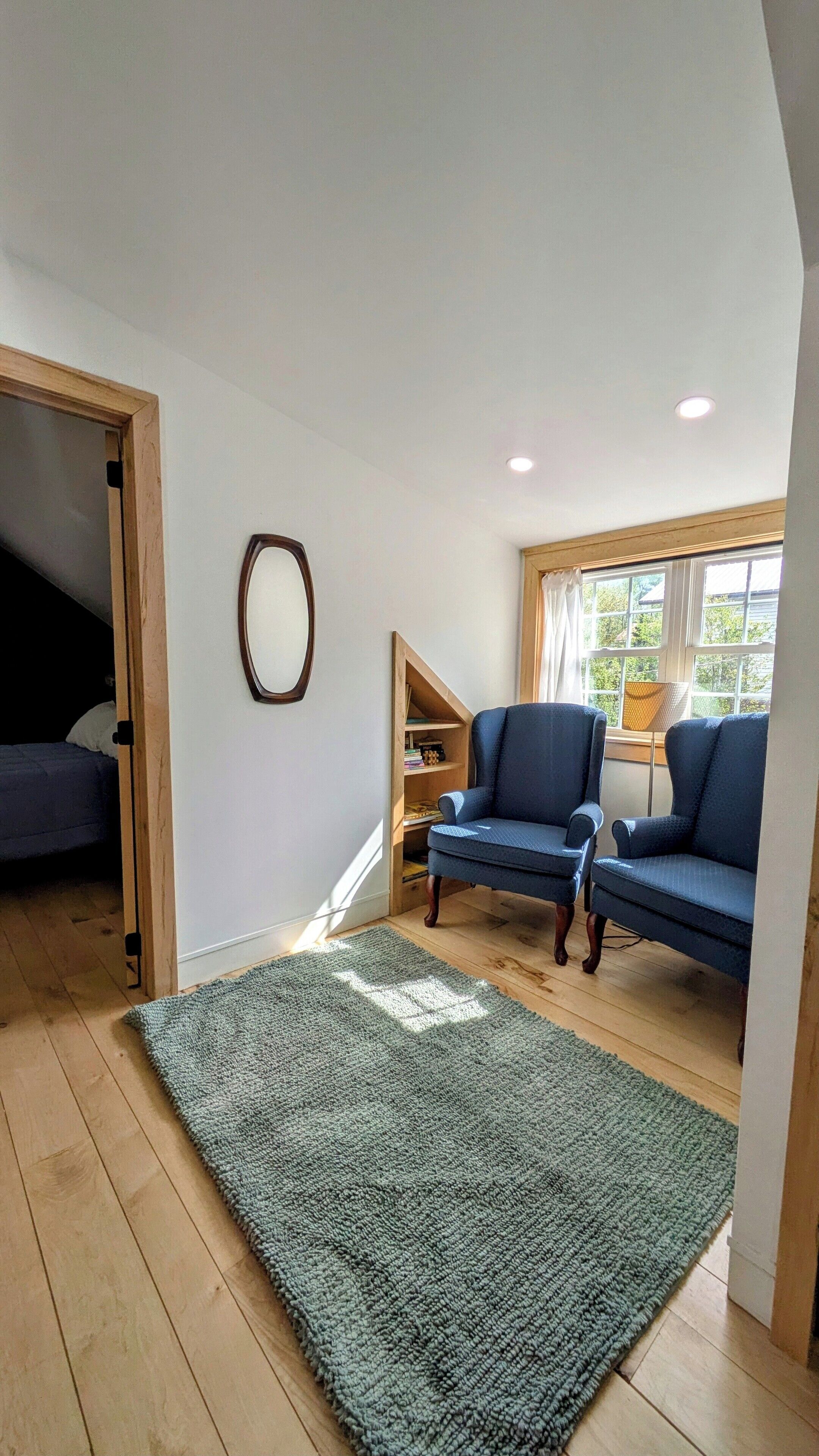 A room with a large window, a blue sofa, a wooden floor, and a green rug.