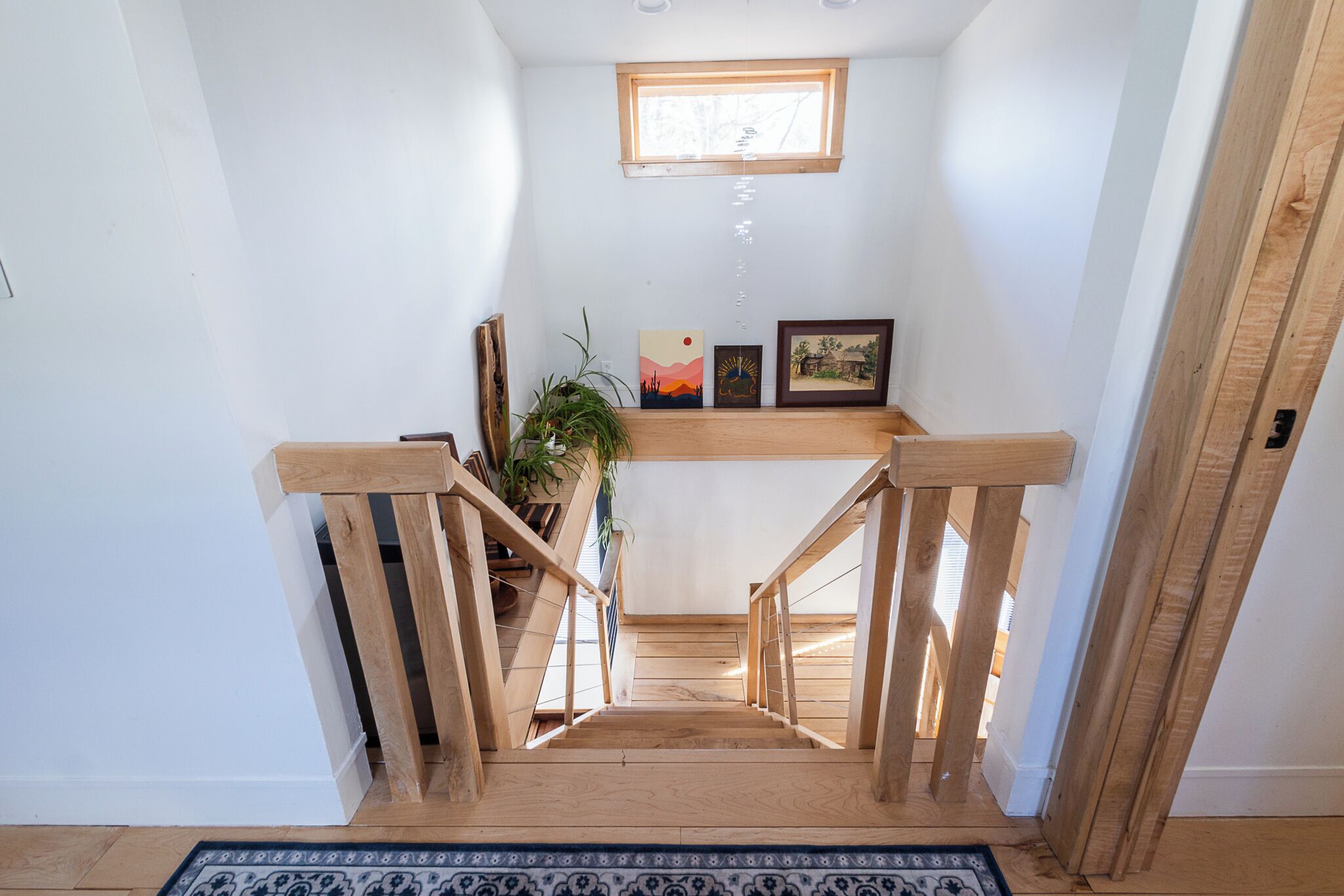 A wooden staircase with a handrail, a small window at the top, and a shelf with framed artwork.