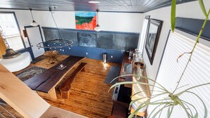 Une pièce avec un plancher en bois, une grande fenêtre, un luminaire suspendu et un tableau au mur.