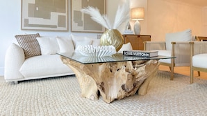Un salon avec une table basse en verre, un canapé blanc et une table d’appoint en bois sur laquelle se trouve une lampe.