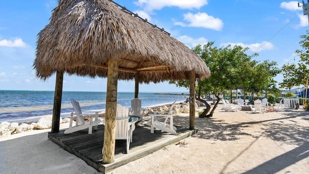 Un belvédère au bord de la plage, avec des chaises blanches, une terrasse en bois et une vue sur l’océan.