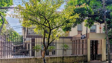 Zona residencial con entrada protegida por una reja, un árbol en primer plano y un edificio con puerta y ventana a la vista.