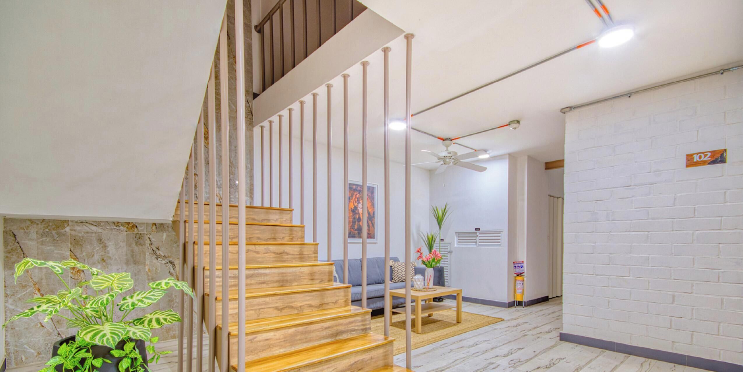 Eine Treppe mit Holzstufen und Metallgeländern, ein Deckenventilator, ein Sofa, ein kleiner Tisch und eine Pflanze.