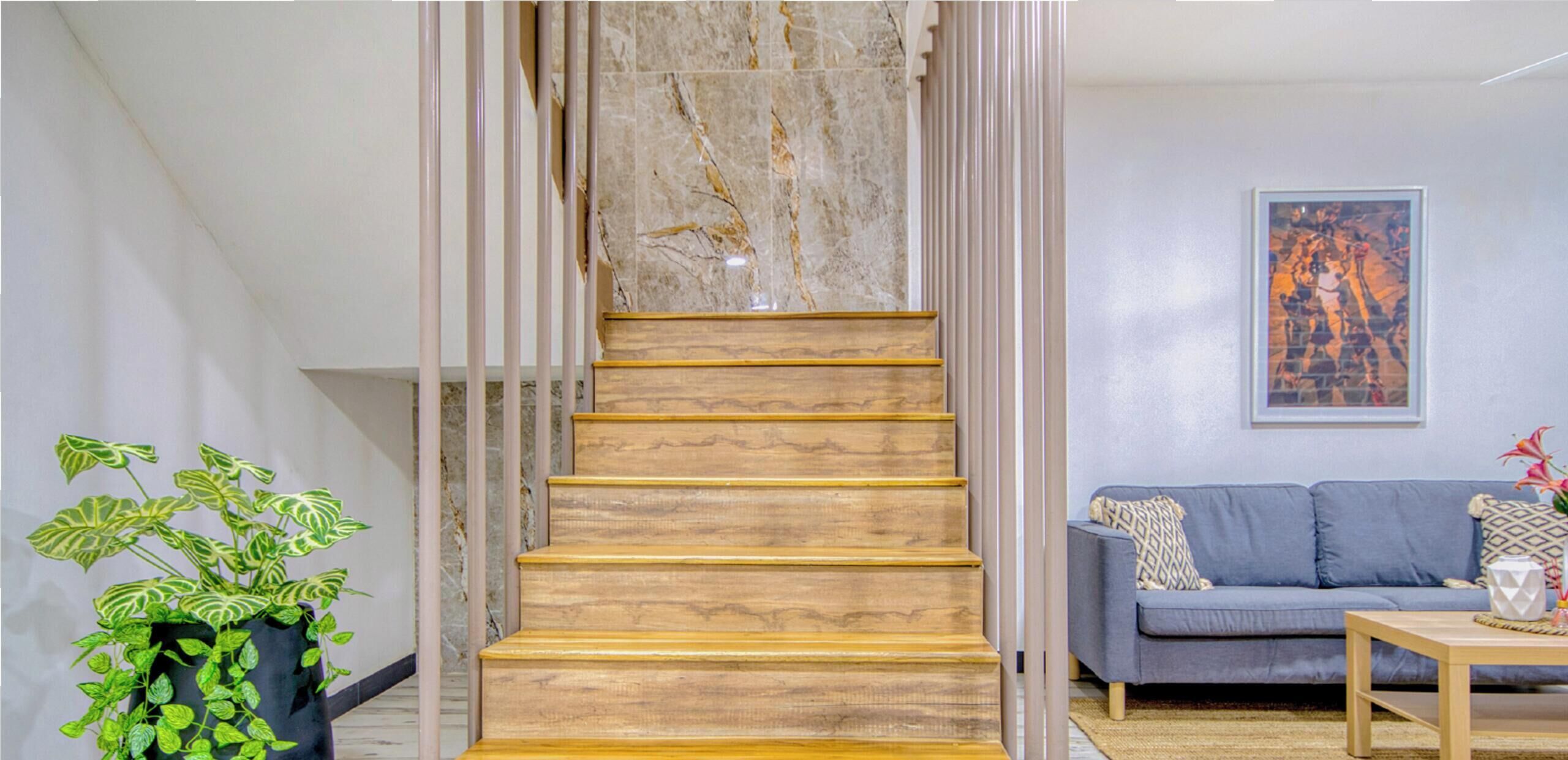 Una escalera con peldaños de madera que conduce a una pared de mármol, un sofá gris y una planta en maceta.