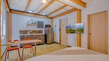 Una habitación compacta con cama, una mesa de comedor con sillas, una kitchenette y un televisor montado en la pared.