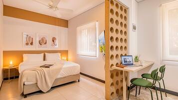 A modern bedroom with a bed, bedside tables, a desk with a laptop, a chair, and a decorative wall panel.