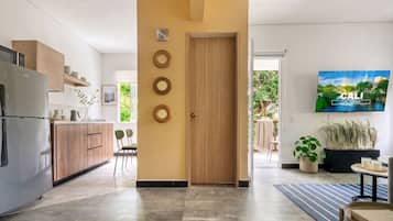 Una cocina moderna con puerta de madera, un comedor con sillas y un televisor mostrando un paisaje urbano.