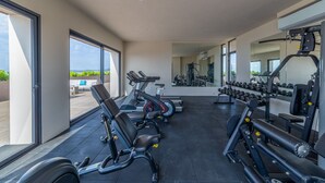 Une salle de sport moderne, équipée de matériel d’exercice, dotée de grandes fenêtres et offrant une vue sur la verdure environnante.