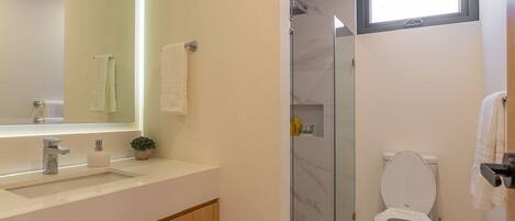 A modern bathroom with a large mirror, a sink, a toilet, and a shower area.