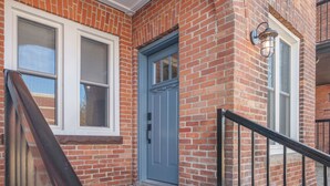 A brick building with a blue door, a window, and a black railing.