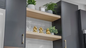 A kitchen with grey cabinets, a wooden shelf, and decorative items including golden figurines, wine glasses, and plants.