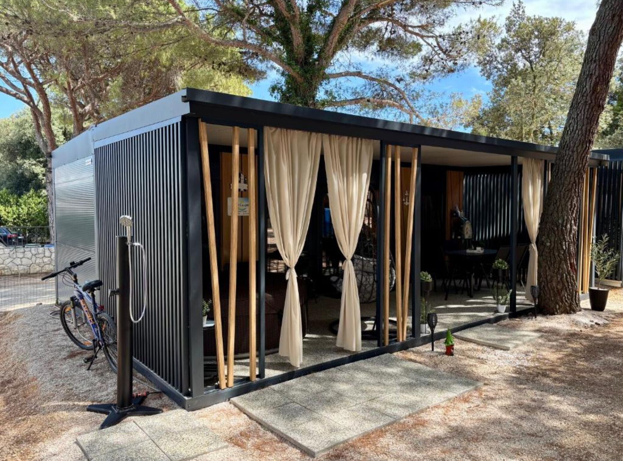 A modern, compact building with a covered outdoor seating area, a bicycle parked outside, and a tree nearby.