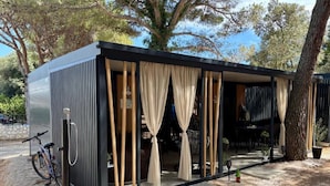 A modern, compact building with a covered outdoor seating area, a bicycle parked outside, and a tree nearby. - TJ Escape - Mobile Home With Hot Tub And Terrace (Pakoštane)