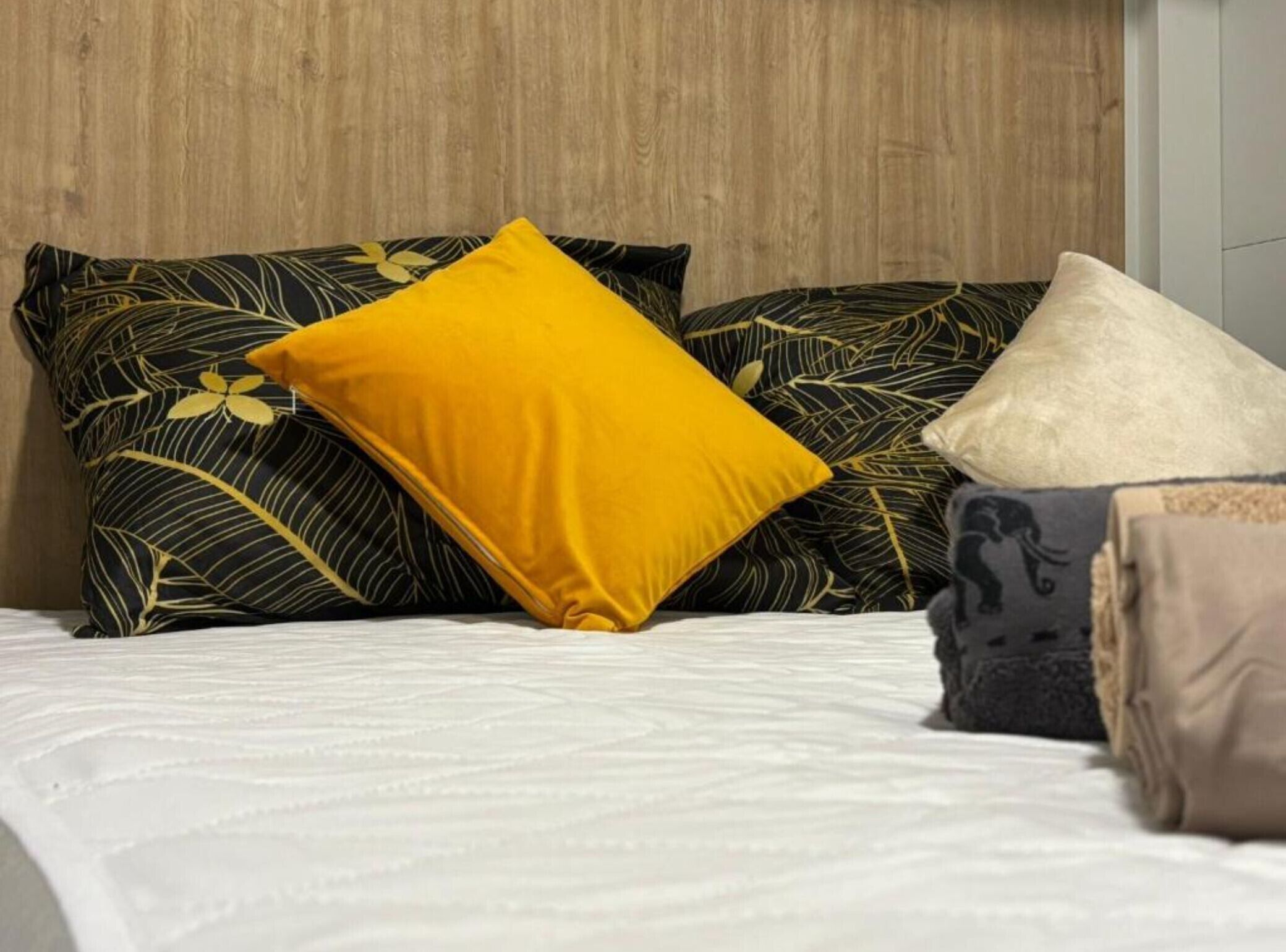 A bed with a white bedspread and three pillows with different patterns and colors.