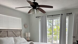 A bedroom with a large bed, a ceiling fan, a window with curtains, and a wooden headboard. - Alamanda Villas (Holmes Beach)