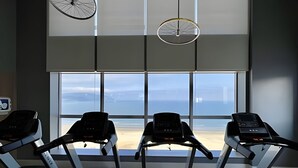 Ein Fitnessraum mit Laufbändern vor einem großen Fenster mit Blick auf einen Strand.